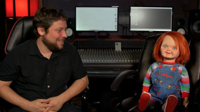 Alex Vincent sits in an audio studio next to the Chucky doll in Living with Chucky.