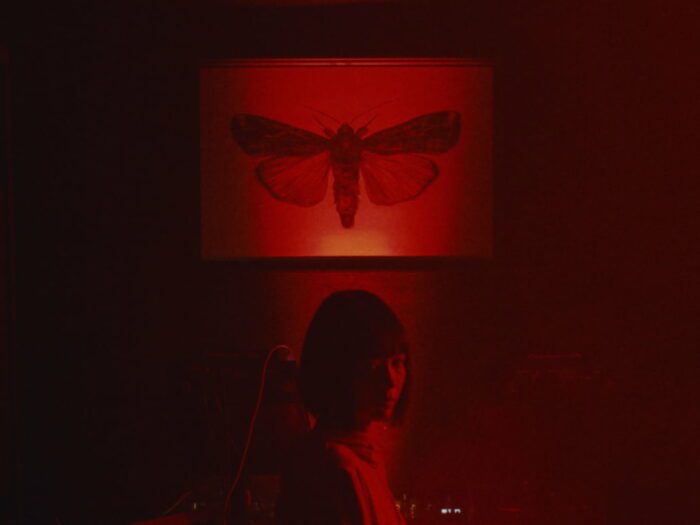 A woman in a red room sits below a picture of a butterfly