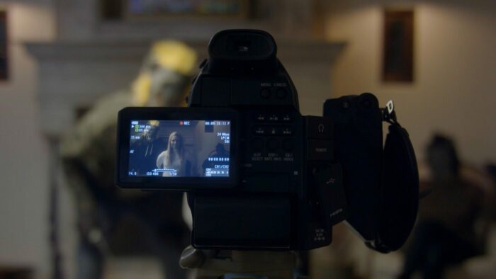 A camera screen shows a masked individual posing beside a woman gagged with duck tape and tied up to a chair.