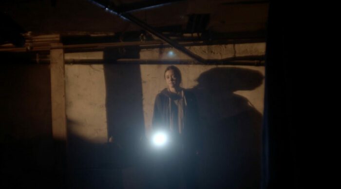 A woman holds a flashlight toward the camera in Morse Code
