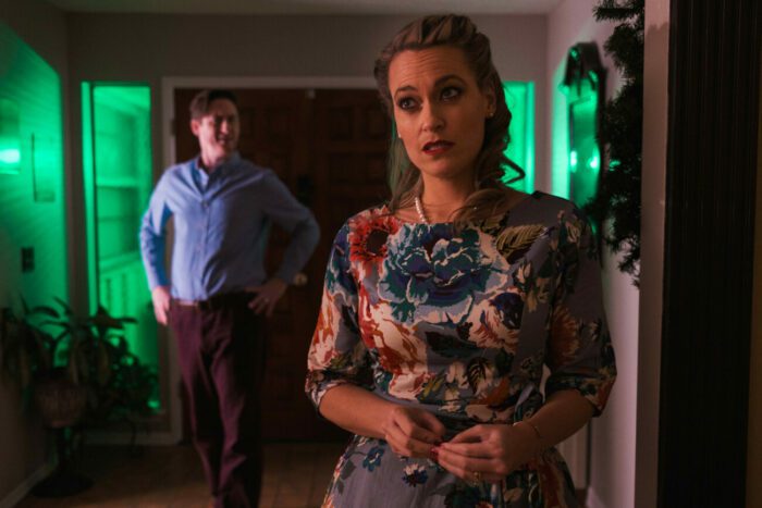 A green glow eminates from behind a man with his hands on his hips and a woman with an unsure look on her face