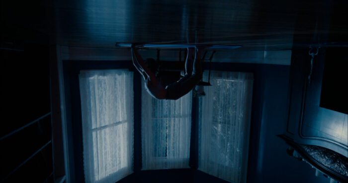 A figure is arched on all fours in a yoga pose in front of windows in a darkly lit room in Mind Body Spirit