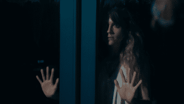 Eva with her hands pressed up against a pair of glass doors