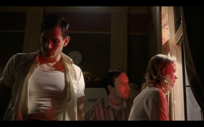 A man and woman look out a window into the red tinted city while another man looks away