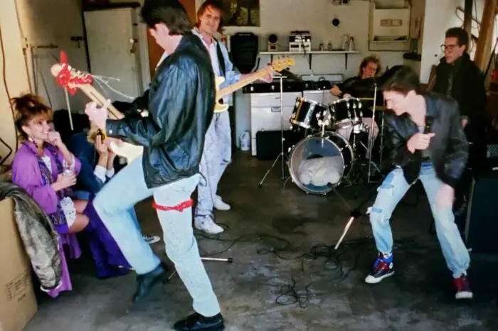 Nikki McQueen, Gary Hays, Greg Joujon-Roche, Robert D. Peverley, Bryan Kovacs, Martin Hansen, Tom Shell in Hard Rock Nightmare (1988). Scene features them as the band Bad Boys practicing in a garage. Screen capture off Shudder.