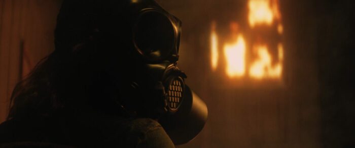 A person in a gas mask outside of a building on fire in American Meltdown