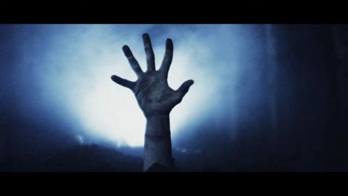 A hand pops up from the ground and is backlit by a harsh light