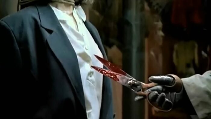 The killer holds up a bloody knife to Betty who is tied up