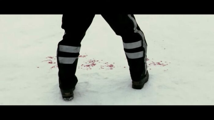 A man stands in a vast field of snow as a line of blood cuts through the snow