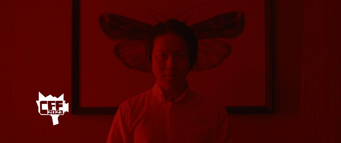 Oka stands in front of a photo of a moth in a red room in New Religion