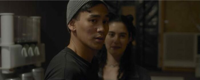 Lee stands in front of Jamie, both are looking toward the camera in Bliss of Evil