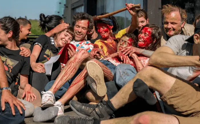 The cast of Final cut crowd together, bloody,smiling, and laughing, one woman has an ax sticking out of her head.