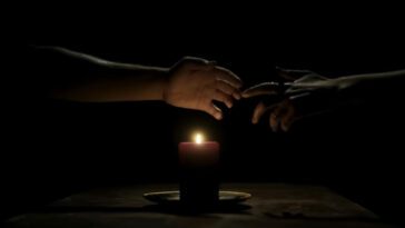 A pair of hands reach out towards each other in the dark.