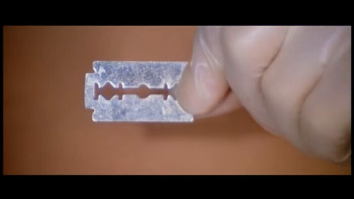 The killer holds a razor blade over Kitty's stomach