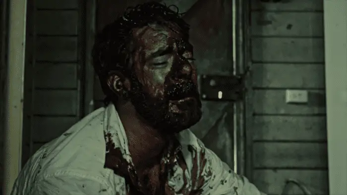 Jack sits on the ground of a dingy building, his entire face and chest are covered in blood