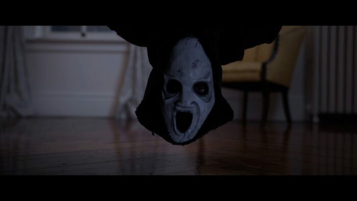 A man with an upside down mask on peaks under the bed