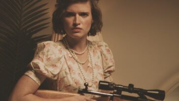 A curly haired woman holds a scoped rifle in a sepia toned photo