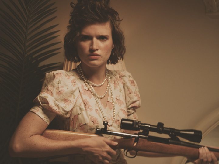 A curly haired woman holds a scoped rifle in a sepia toned photo