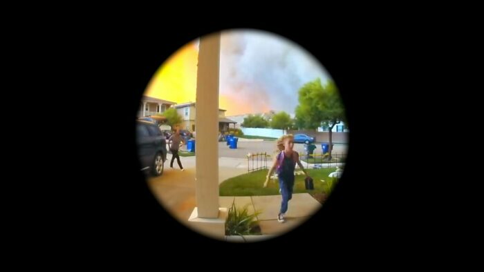 A fire blazes behind a home while a woman packs her car trunk and a young girl walks toward her home in Home Invasion
