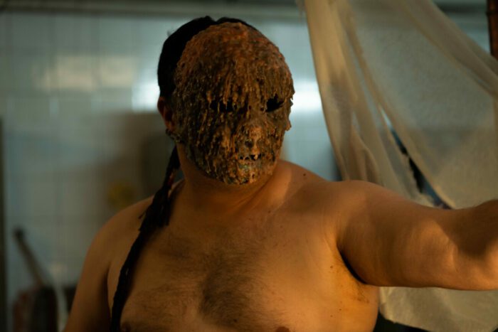 a naked man in a wax dripped mask