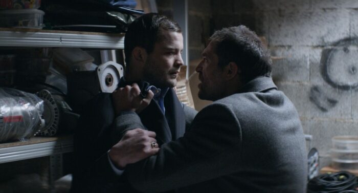 A man holds another man up against a wall