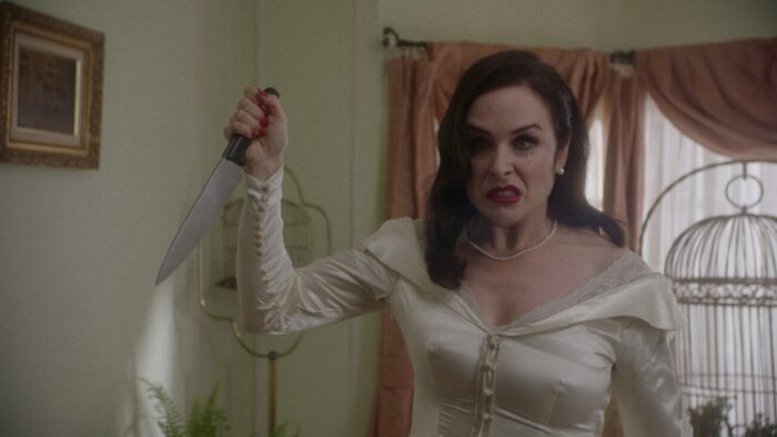 a woman in a white dress raises a knife in a hallway
