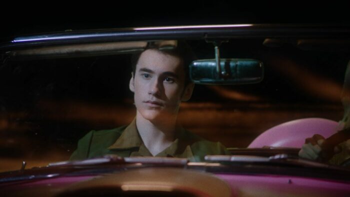 A man sitting in a pink convertable seen through the windshield