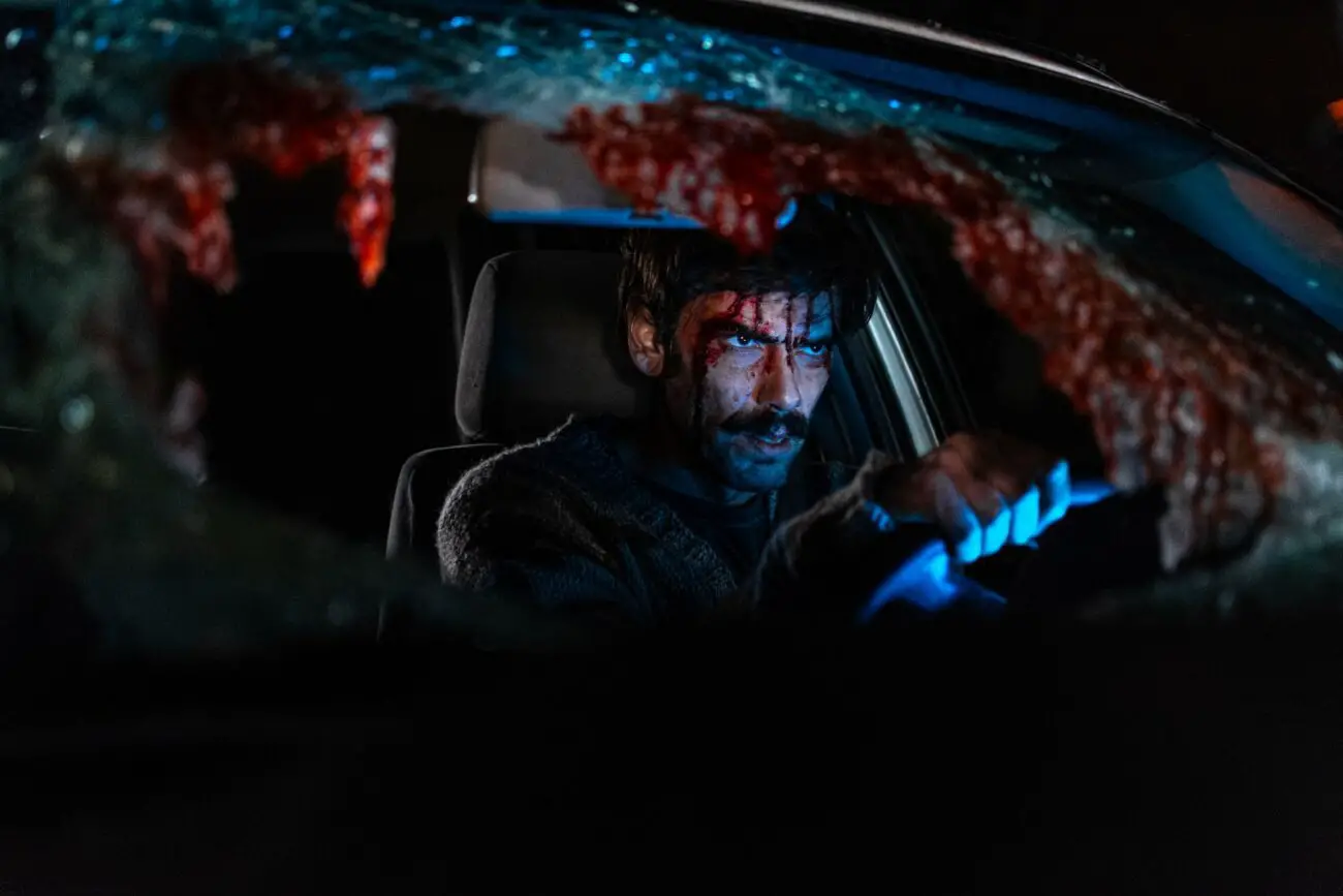 A bloodied man in a car with a shattered windshield