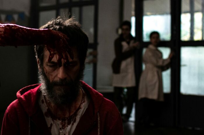 A hand smearing blood on a man's forehead