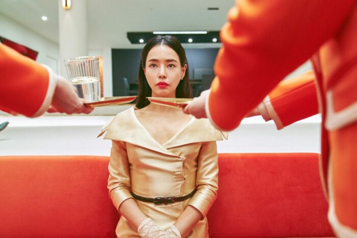 Yeo-rae sits on a red couch as plates are being offered to her