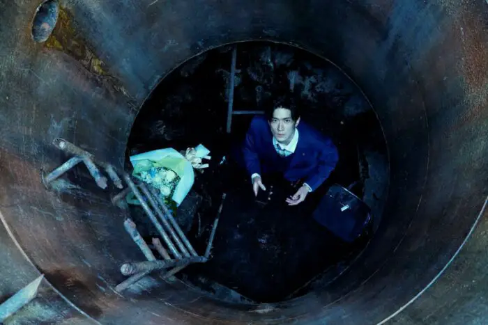 Shunsuke stands at the bottom of a manhole. and looks up towards the sky