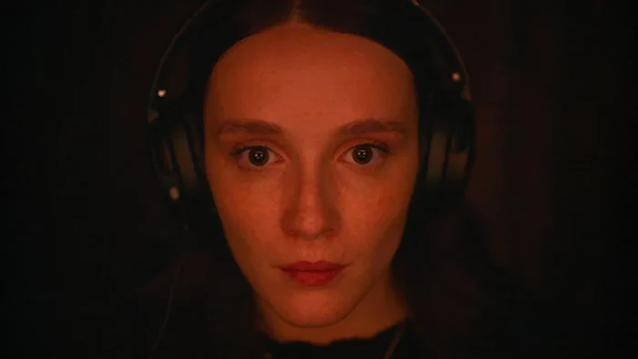 A woman gazes intently into a computer screen with a red glow cast on her face.