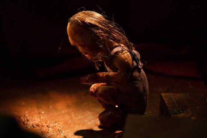 A small, wax figure crouches, its face partially in shadow.