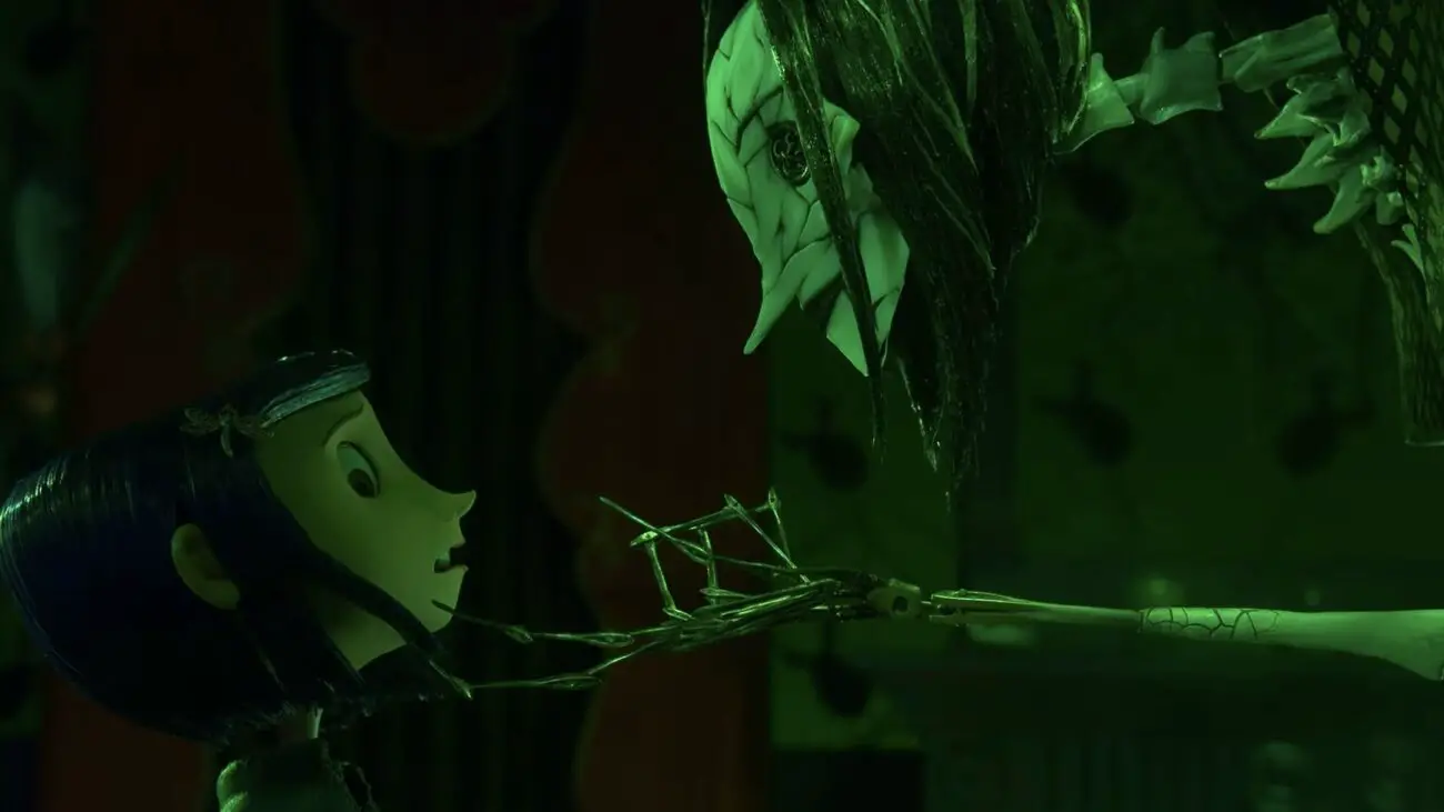Coraline faces the Other Mother in her true form, a skeletal and menacing figure with cracked skin and button eyes. The Other Mother's long, skeletal fingers reach towards Coraline in a dark, eerie setting lit with green light.