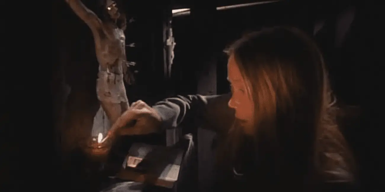 A scene from "Carrie" (1976), featuring Sissy Spacek as Carrie White lighting a candle before a crucifix in her dimly lit room. The image highlights the religious overtones and the oppressive atmosphere of her home.