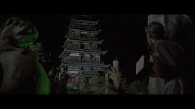 A traditional Chinese castle looms in the dark. A peasant stands in front of it with a hand-plow. The door at the base glows green with ominous light.