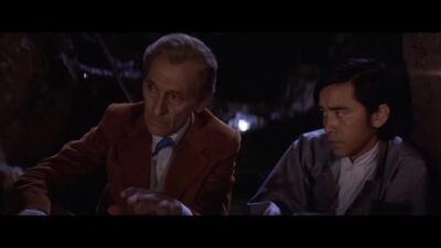 Two men sit by a fire, talking.